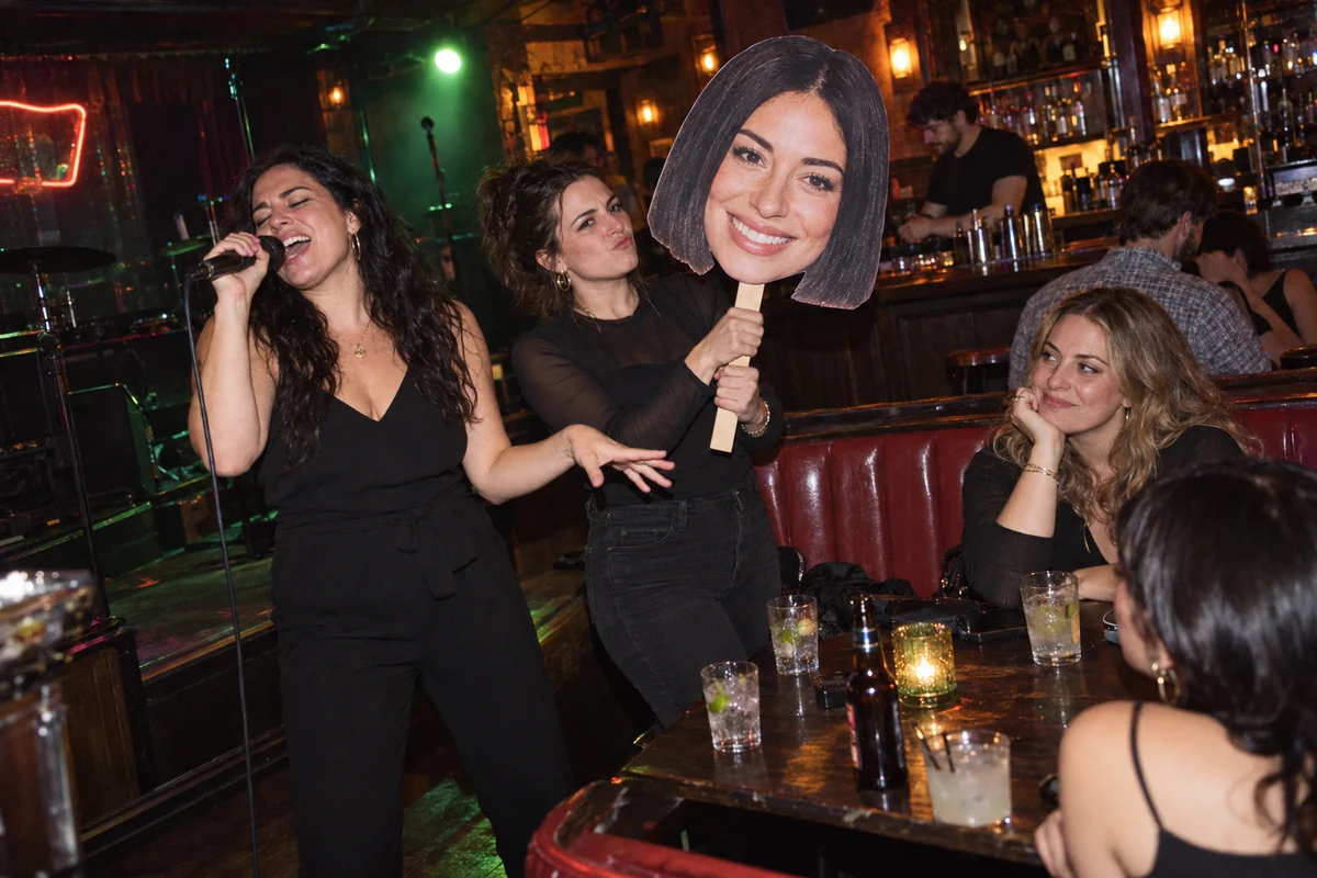 Friends singing karaoke with a bride head sign in a neighborhood bar